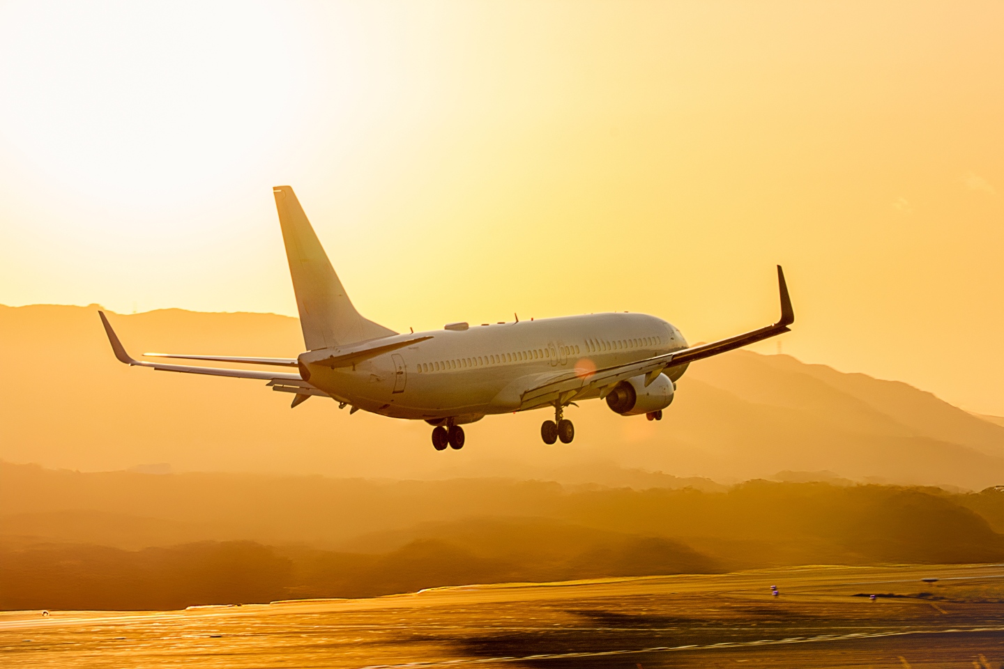 Avion de ligne à l'atterrissage au coucher du soleil au-dessus de collines boisées